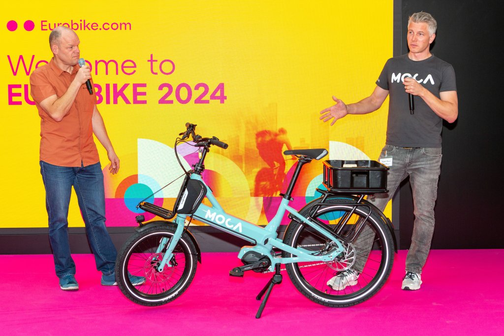 Zwei Männer präsentieren auf einer Bühne ein Cargobike.