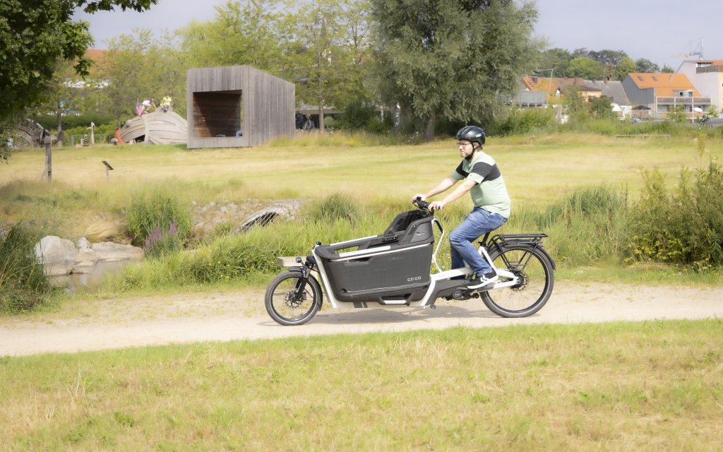 Mann fährt auf Lastenrad durch einen Park.