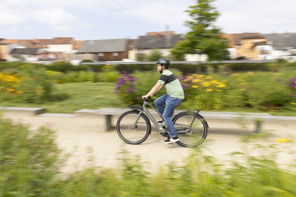 Mann fährt mit E-Bike durch einen Park mit Blumen.