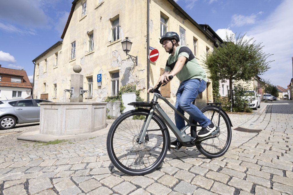 Mann fährt mit E-Bike an einem Brunnen vorbei.