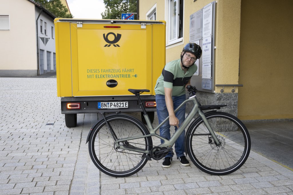 Mann steht mit E-Bike vor einem Postfahrzeug.