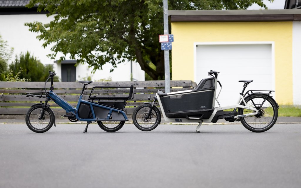 Ein Long-John- und ein Longtail-Lastenrad stehen auf einer Straße.