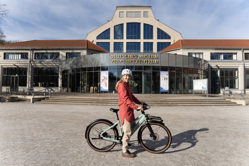 Frau steht mit City-E-Bike vor einem Museum.