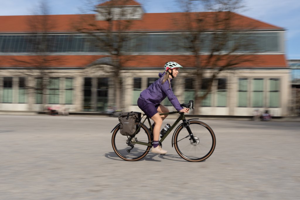 Frau fährt auf Gravelbike mit Taschen über einen Platz.