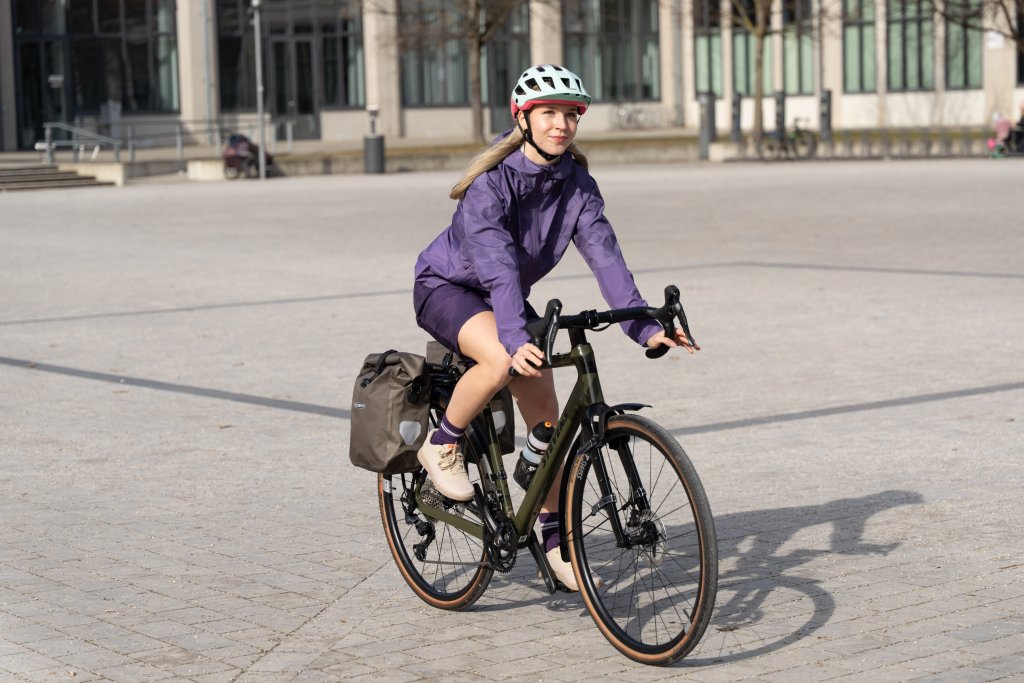Frau fährt auf Gravelbike über einen sonnigen Platz.