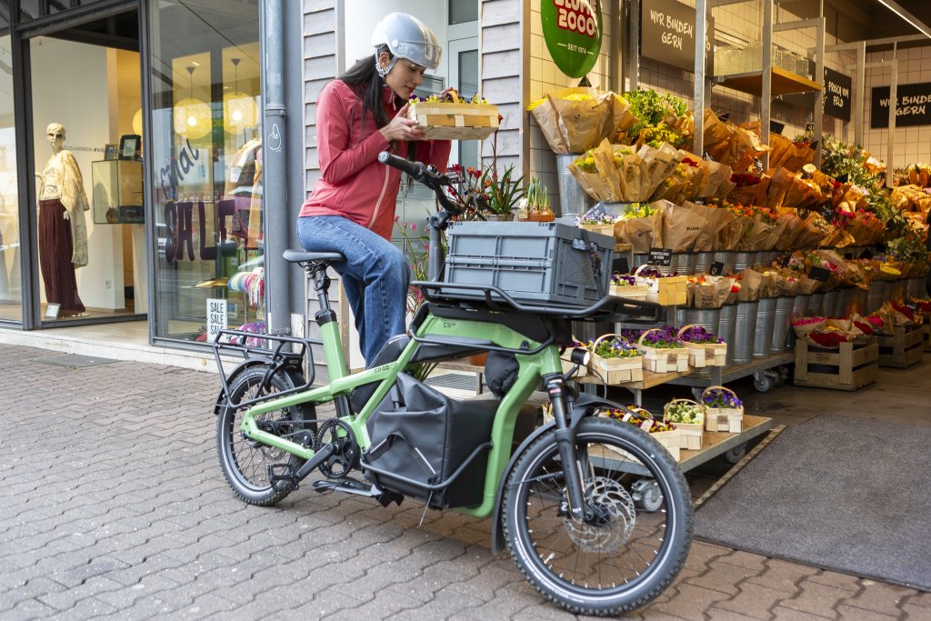 Frau steht mit Cargobike vor einem Blumenladen.