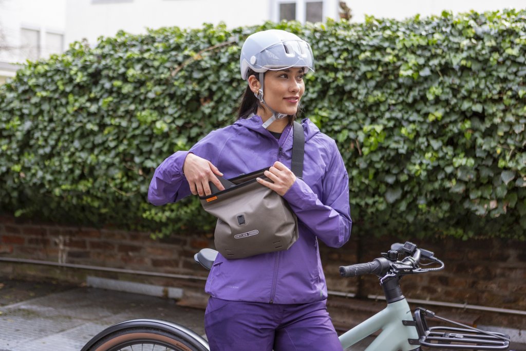 Frau steht mit Umhängetasche am Fahrrad.