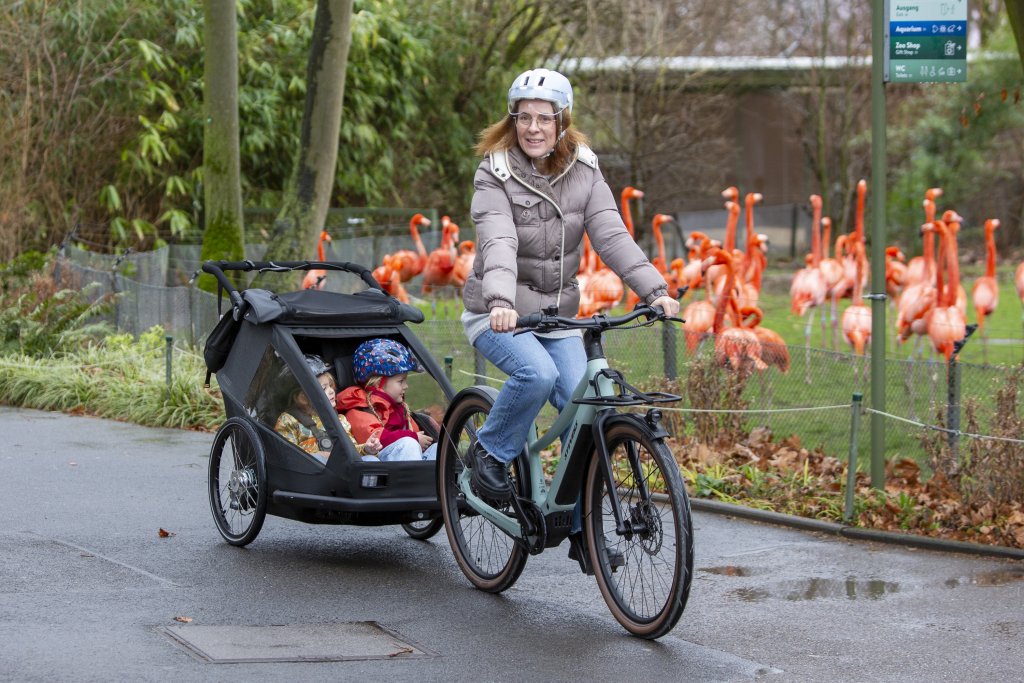 Frau fährt mit E-Bike und Kinderanhänger durch einen Zoo.