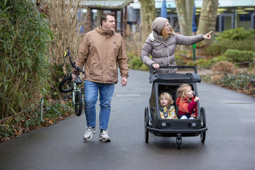 Familie schiebt einen Kinderanhänger mit zwei Kindern durch einen Zoo.