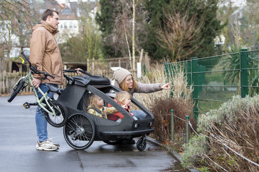 Familie steht mit Kinderanhänger in einem Zoo.