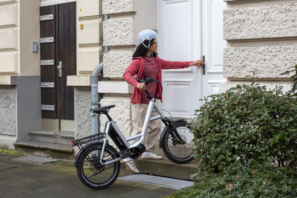 Frau steht mit einem E-Bike vor einer Haustür.