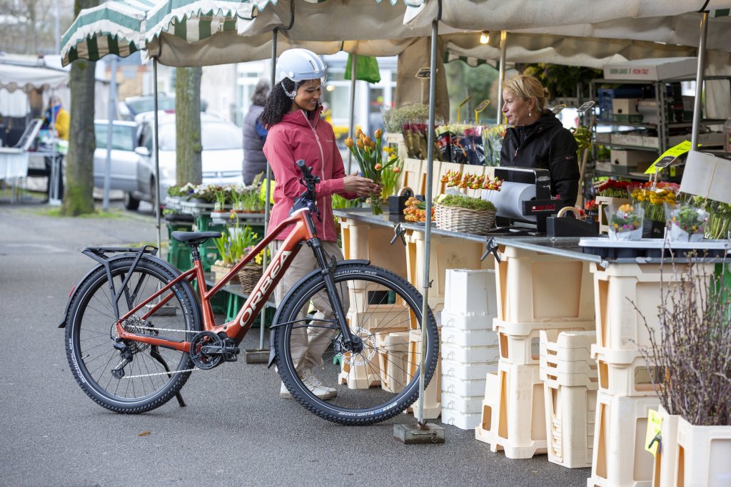 Frau steht mit E-Bike an einem Marktstand.