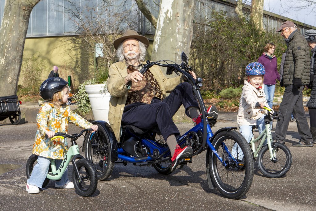 Senior und Kinder fahren mit Fahrrädern durch einen Park.
