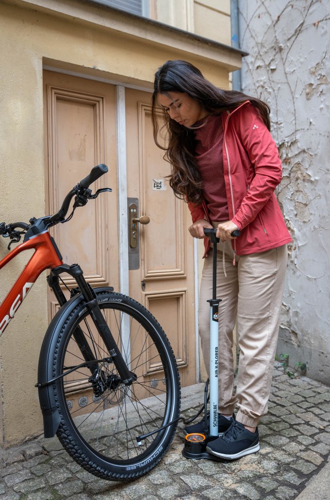 Frau pumpt Reifen von E-Bike mit einer Luftpumpe auf.