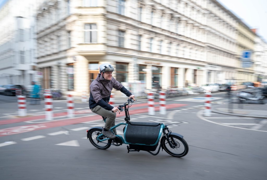 Mann fährt mit Lastenrad durch eine Stadt.