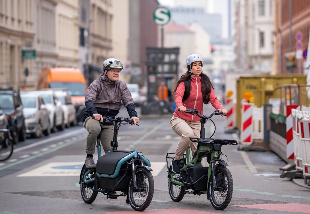 Frau und Mann unterwegs mit jeweils einem Lastenrad in einer Stadt.