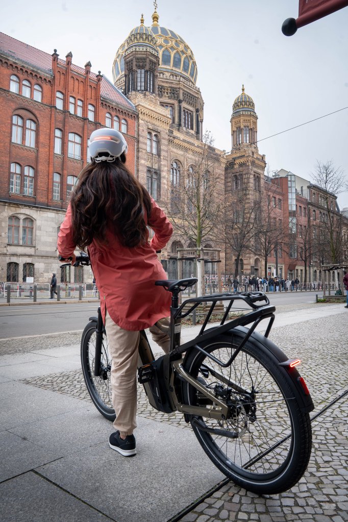 Frau fährt mit einem E-Bike aus einer Einfahrt auf die Straße.