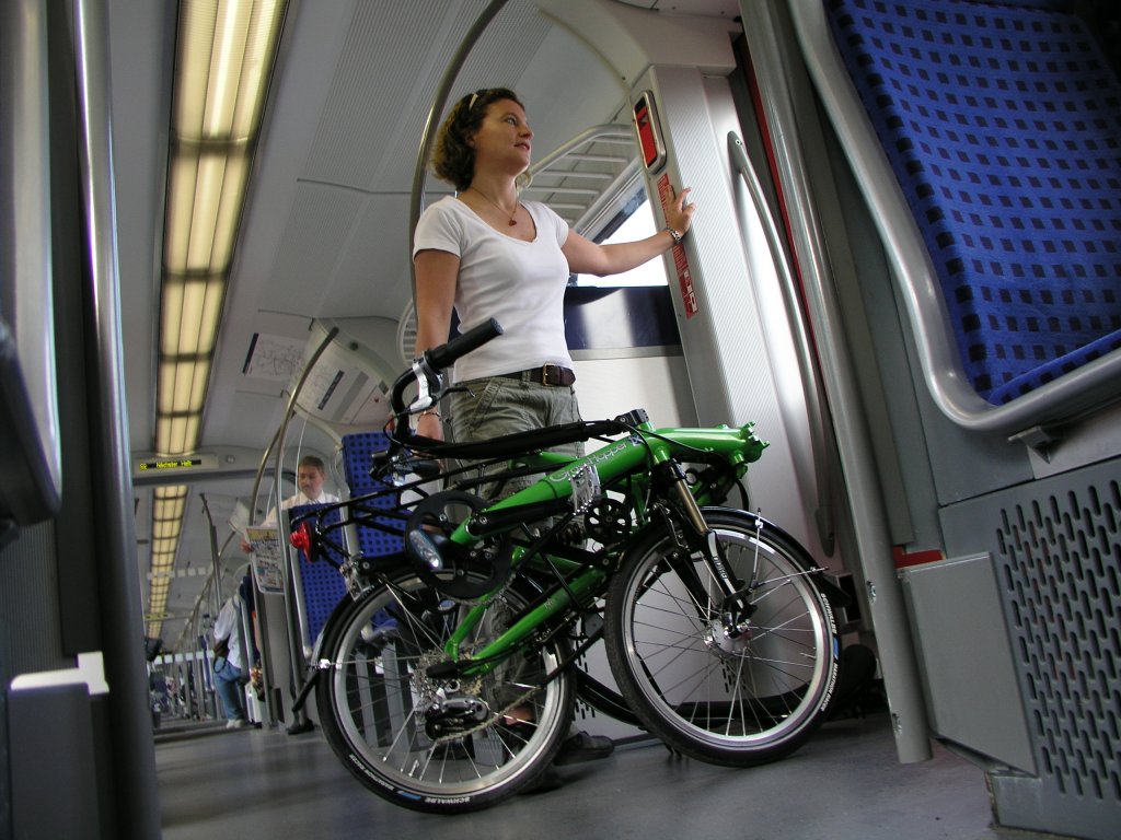 Eine Frau mit einem zusammengeklappten Liegerad in einem Zug.