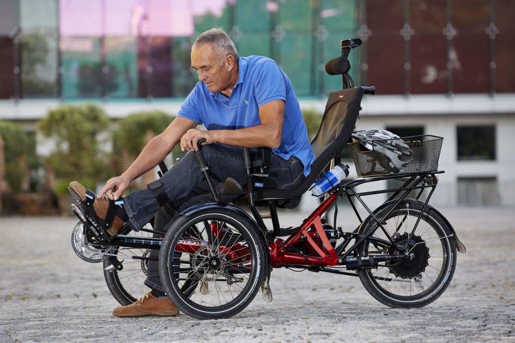 Ein Mann fixiert seine Schuhe auf dem Pedal eines Liegedreirads.