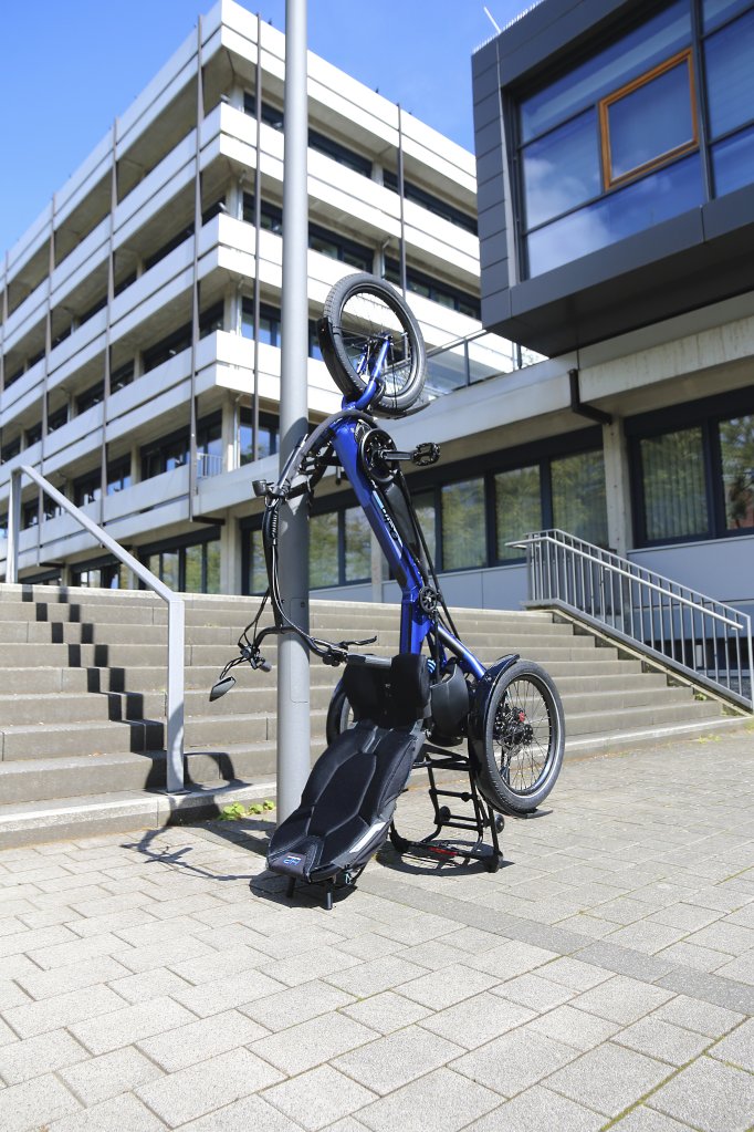 Das Foto zeigt das Sesseldreirad „Delta tx“ von HP Velotechnik, das aufrecht vor einer Treppe geparkt wurde.