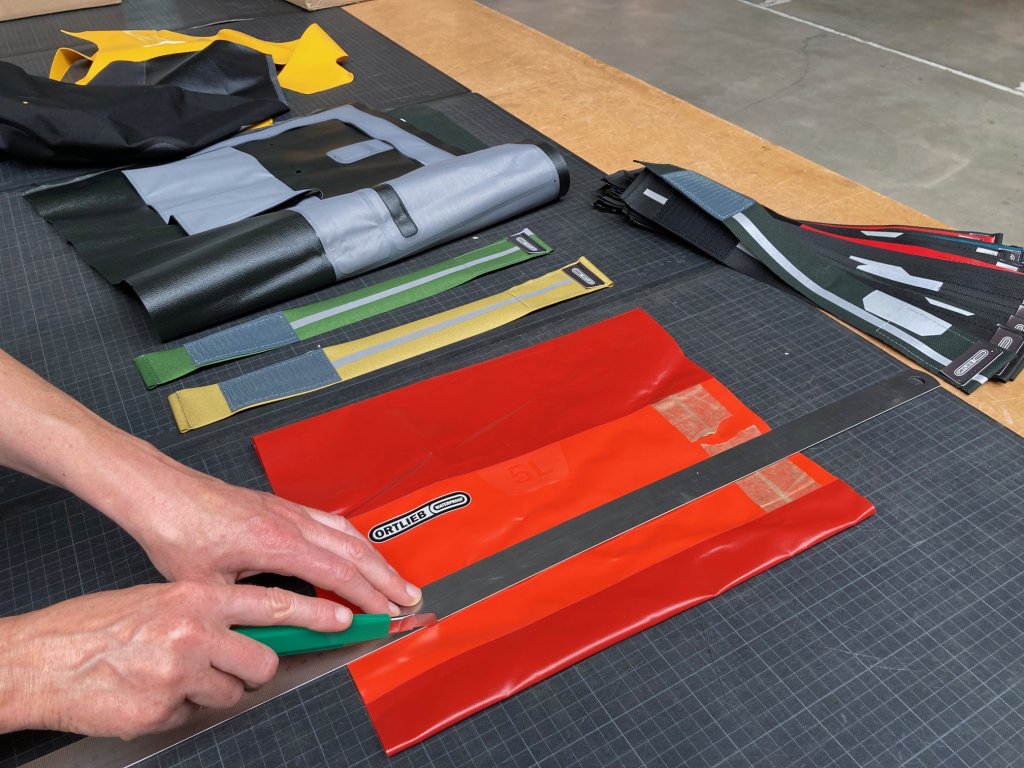 Eine Person schneidet mit einem Arbeitsmesser und einem Metalllineal Materialien einer Fahrradtasche.