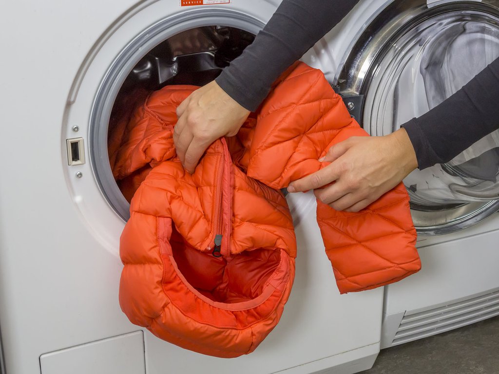 Eine Person steckt eine wattierte Jacke in eine Waschmaschine.