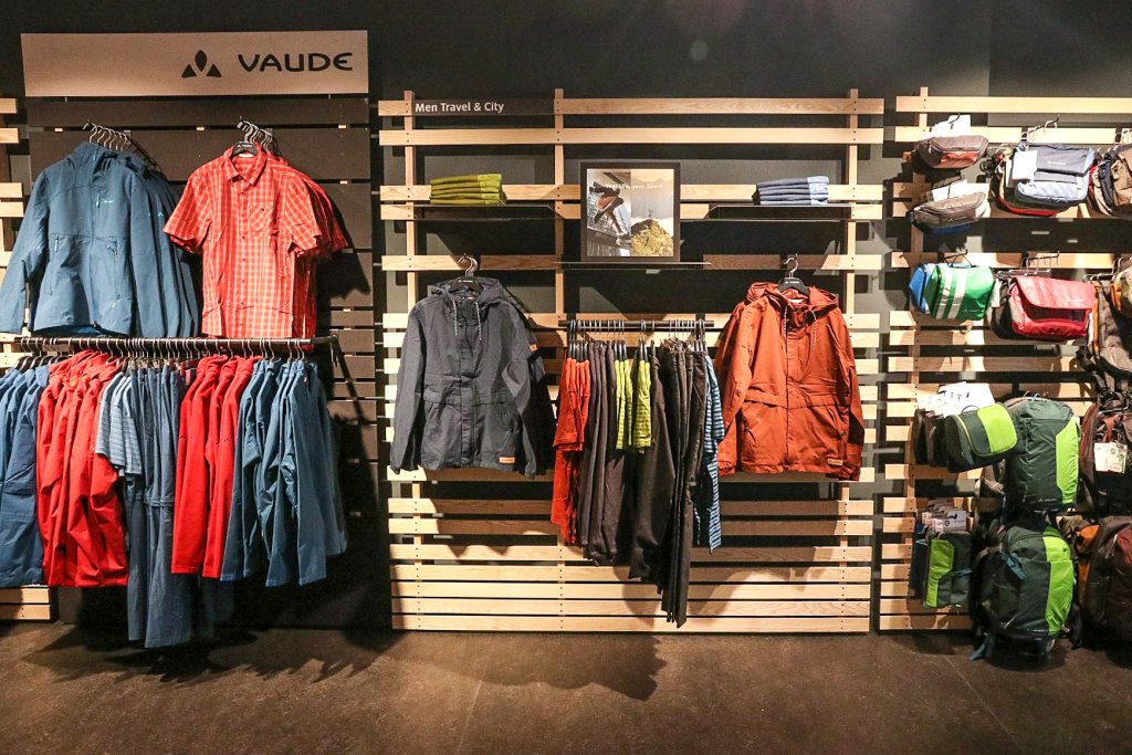 Eine Produktpräsentationswand mit Jacken, Oberteilen und Taschen der Firma Vaude.