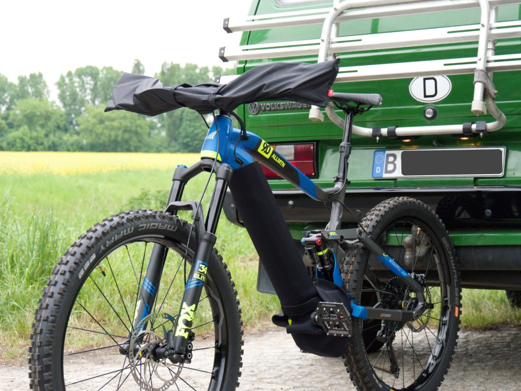 Ein E-Bike steht vor einem Kleinbus. Ãœber dem Lenker ist eine Schutzhülle.