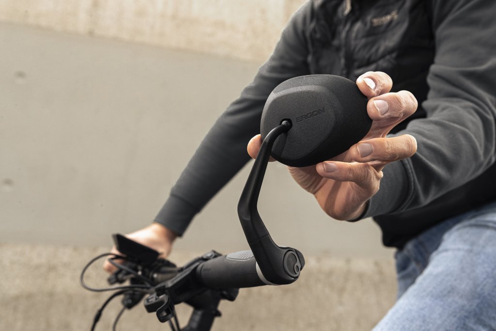 Eine Person stellt mit der linken Hand den Rückspiegel an einem Fahrradlenker ein.