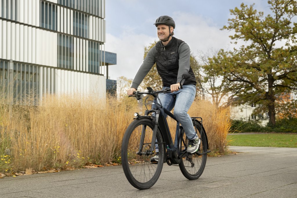 Ein Mann fährt auf einem E-Bike an einem Gebäude mit trockener Bepflanzung davor vorbei.