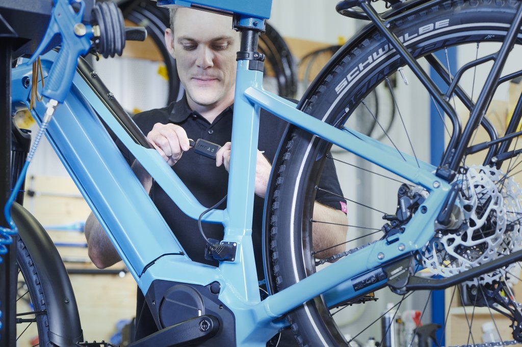 Ein Mann hantiert in einer Werkstatt an einem Kabel, dass an einem E-Bike angeschlossen ist.