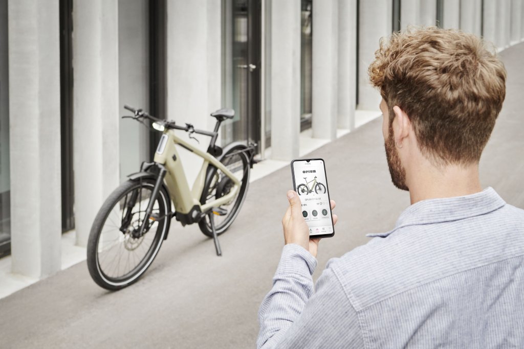 Blick über die Schulter eines Mannes, der auf ein Smartphone schaut. Im Hintergrund steht ein E-Bike vor einem Gebäude.