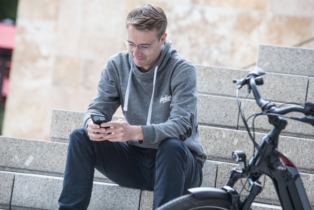 Mann sitzt mit Smartphone auf Treppe.