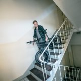 Ein Mann trägt ein E-Bike die Treppe in einem Wohnhaus hinunter.