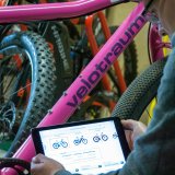 Eine Person hält ein Tablet vor den Rahmen eines Fahrrades. Auf dem Display sind kleine Abbildungen von Fahrrädern zu sehen.