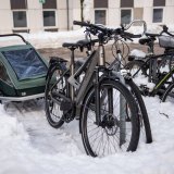 Ein Fahrrad mit Anhänger an einem Abstellbügel. Im Bereich der Stellfläche liegt weniger Schnee als daneben.