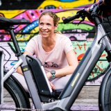 Eine Frau sitzt lächelnd hinter einem abgestellten E-Bike.
