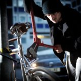 Ein Mann setzt einen Bolzenschneider an einem Bügelschloss an, mit dem ein Fahrrad an einem Metallpfosten gesichert ist.