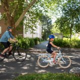 Ein Mann und ein Kind fahren auf Fahrrädern eine Straße zwischen Wohnhäusern entlang.