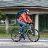 Eine Frau mit einem Rucksack fährt auf einem Fahrrad auf einem Radweg in der Stadt.