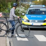 Eine Person schiebt ein Fahrrad über einen Fußgängerüberweg und schaut zu einem Polizeiauto auf der Fahrbahn.