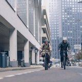 Zwei Personen fahren auf Fahrrädern in einer Großstadt auf die Kamera zu.