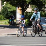 Ein Kind und ein Mann fahren nebeneinander auf Fahrrädern auf einer Straße.