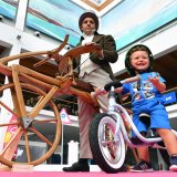 Ein Kind mit einem Laufrad vor einem Mann mit einem historischen Laufrad aus Holz.