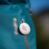 Ein runder Button mit eine:r stilisierten Radfahrer:in an einer Tasche mit dem Logo der Firma Ortlieb.