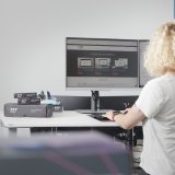 Eine Person steht an einem Schreibtisch mit zwei Computermonitoren und hat die Hände auf der Tastatur.