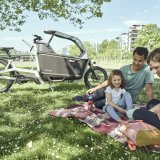 Eine Familie beim Picknick; im Hintergrund steht ein Lastenrad.