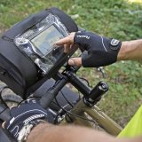 Eine Person tippt mit dem Finger auf das Display eines Smartphones oder Navigationsgeräts in einer Klarsichthülle auf dem Deckel einer Lenkertasche eines Fahrrades.