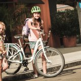Ein Mädchen mit und eins ohne Fahrrad treten vom Gehweg auf die Straße.