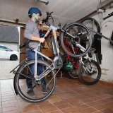 Ein Mann platziert ein E-Bike in einer Garage an einer speziellen Wandaufhängung für Fahrräder.